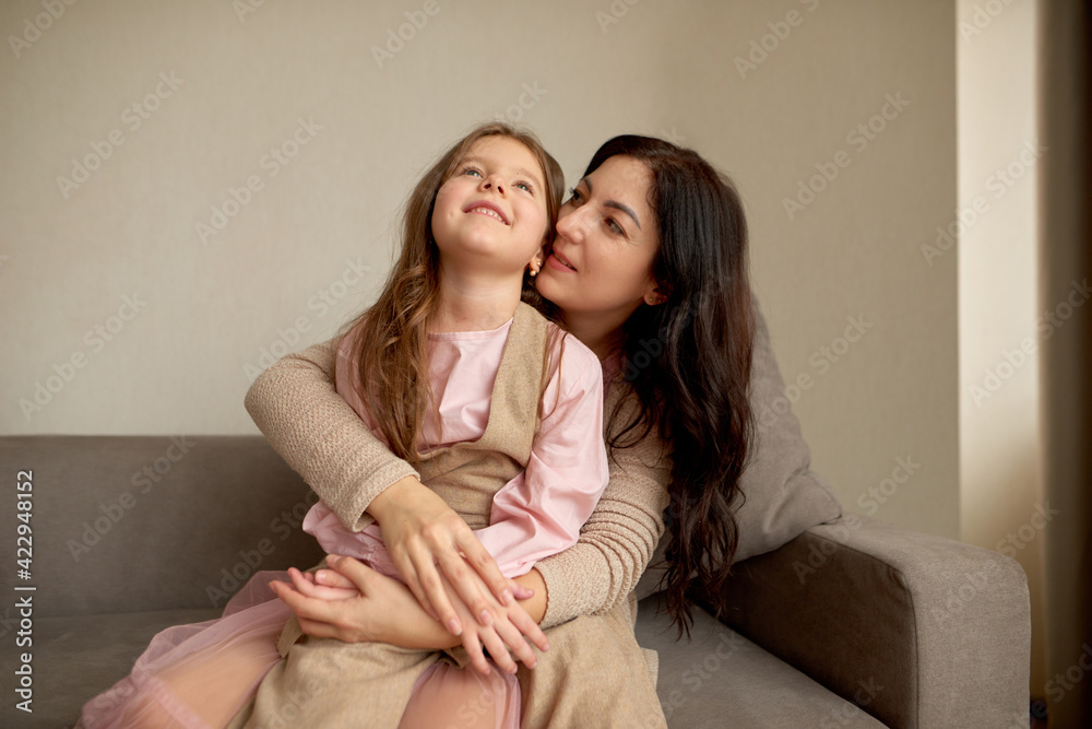 Playful small girl and young happy mother dream together, perfect weekend at home. They are embracing each other tightly with love.