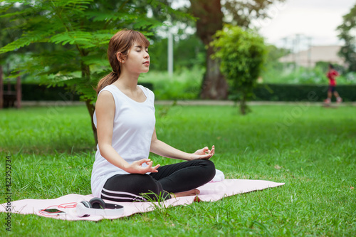 Image of Asian woman sitting and meditation yoga lotus pose outdoor park.