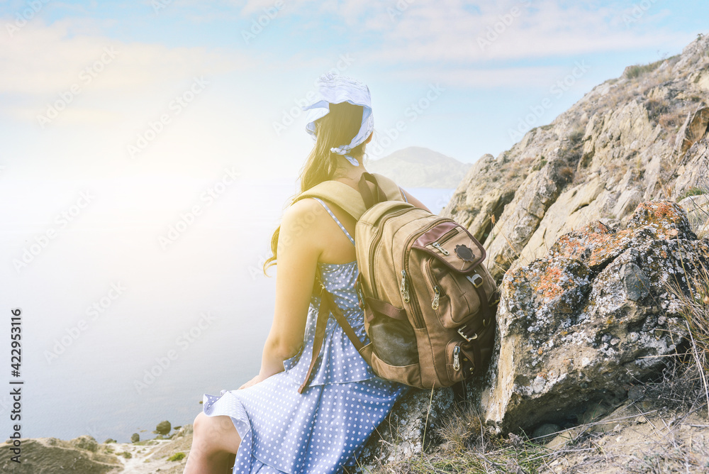 Young girl on vacation. Hiker with a backpack is resting on the top of the mountain and enjoying the view of the sea and mountains. Travel and tourism.