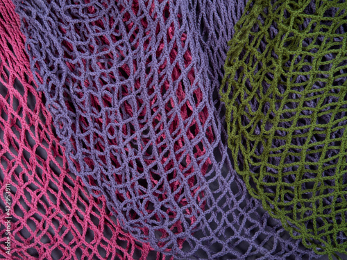 The multicolor background of the zero waste string bags, closeup of the knitted net. Selective focus.