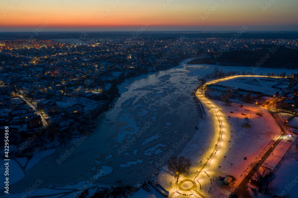Beautiful evening top view of the city. Evening, night illumination in the city. Winter city in the snow. The river is covered with ice.