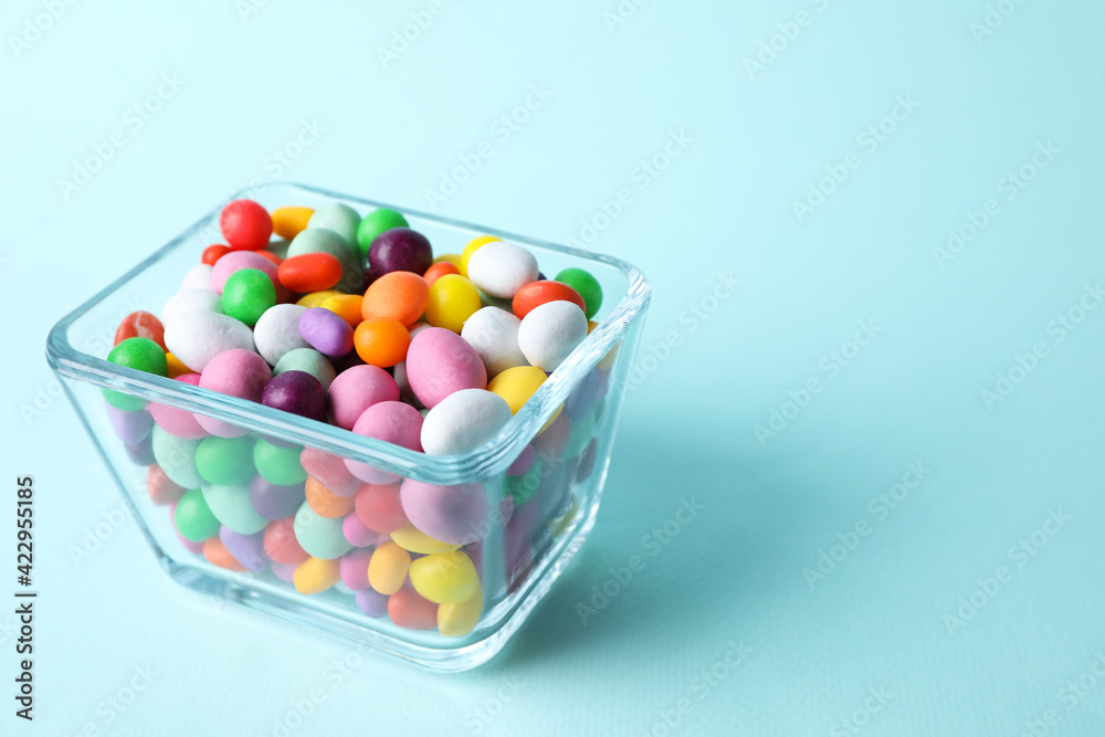 Yummy candies in glass bowl on light blue background, space for text Yummy candies in glass bowl on light blue background, space for text