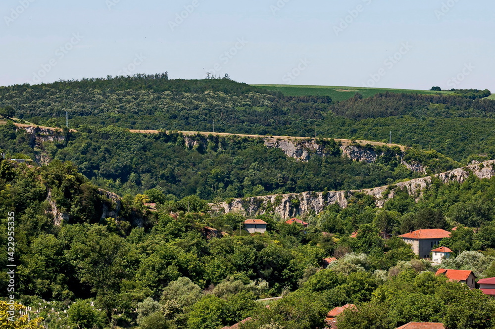 Fototapeta premium View of the beautiful village of Nisovo, Bulgaria, located below, above and in the high limestone cliffs, protected by magnificent deciduous trees