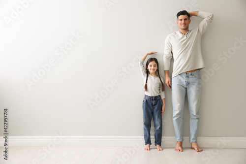 Little girl and father measuring their height near light grey wall indoors. Space for text photo