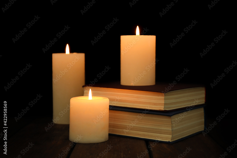 Burning candles and stack of books on wooden table in darkness Burning candles and stack of books on wooden table in darkness