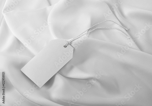 Plain white clothing tag label with hanging thread on white silky fabric photo