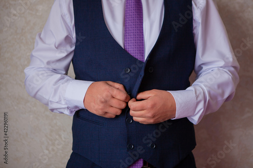 A man's hand buttons a three-piece suit.