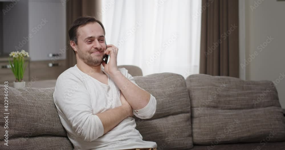 Delighted male speaking on smartphone. Optimistic adult man talking on mobile phone and laughing while relaxing on couch at home Delighted male speaking on smartphone. Optimistic adult man talking on mobile phone and laughing while relaxing on couch at home