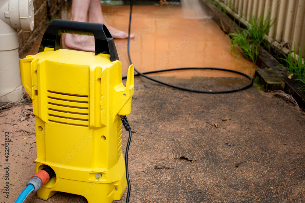 Selective focus. Cleaning backyard paving tiles with high pressure washer.