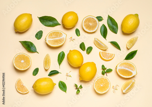 Many fresh ripe lemons with green leaves and flowers on beige background  flat lay