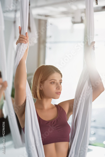 sportive woman looking away while practicing fly yoga with hammock