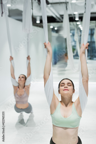 young woman with closed eyes training with aerial yoga strap on blurred background