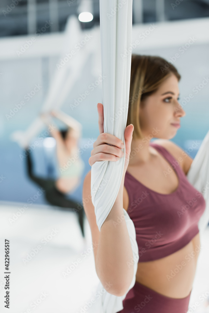 selective focus of young woman warming up with fly yoga strap on blurred background