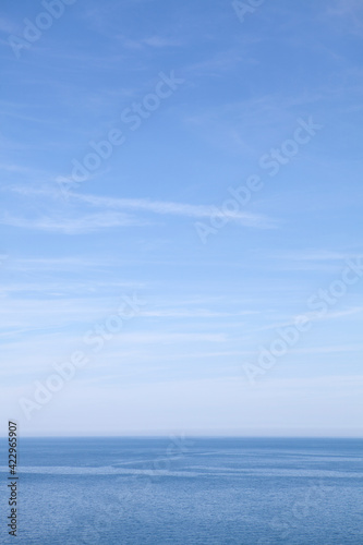 Blue sea and blue sky with wispy white clouds 
