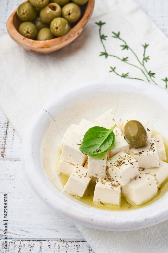 Feta cheese cubes with rosemary, olives and olive oil sauce in white bowl on light gray background. Traditional Greek homemade cheese. Selective focus. Feta cheese cubes with rosemary, olives and olive oil sauce in white bowl on light gray background. Traditional Greek homemade cheese. Selective focus.