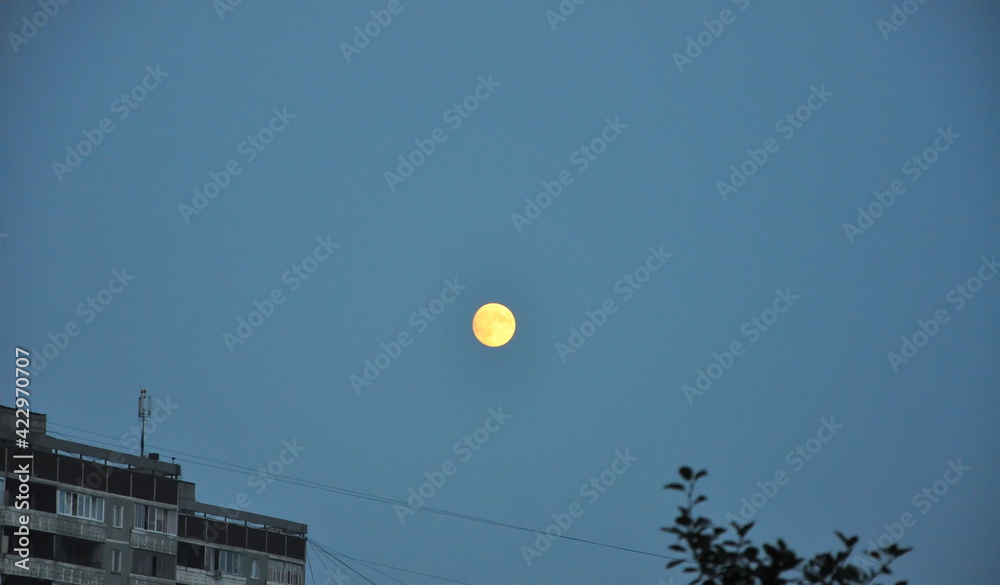 A full moon in the blue night sky above the city houses. A full moon in the blue night sky above the city houses.