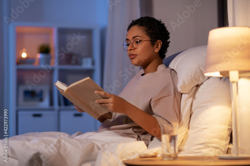 Canvas-taulu young woman in glasses reading book in bed at home