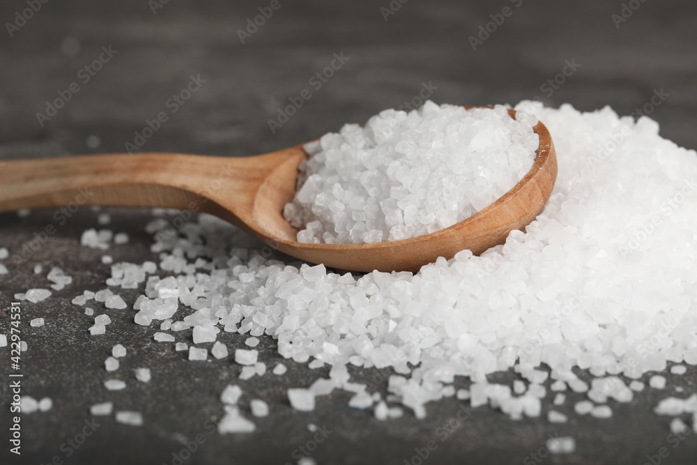 Natural sea salt and wooden spoon on grey table, closeup