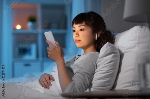 woman with phone and earphones in bed at night