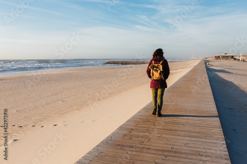 backpacker young caucasian woman relaxing at the beach at sunset. walking by wooden passage or runway. Holidays and relaxation concept