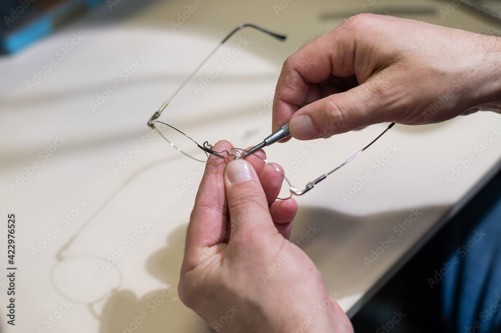 Optical technician fixing glasses. Close-up of male hands with screwdriver and goggles frame. Optical technician fixing glasses. Close-up of male hands with screwdriver and goggles frame.
