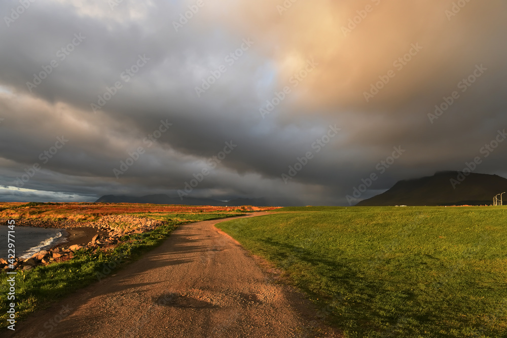 Dirt road by the ocean and dramatic sky at sunset. Iceland, 
