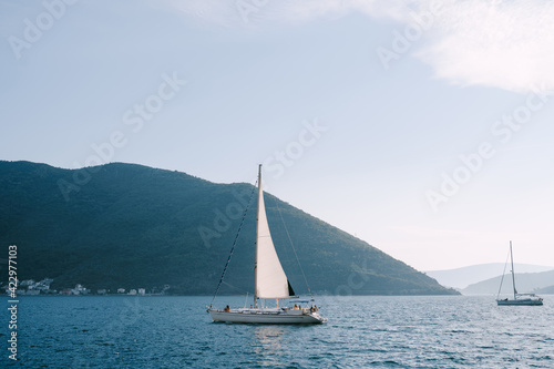 A white sailboat with people floats on the calm water of the bay.