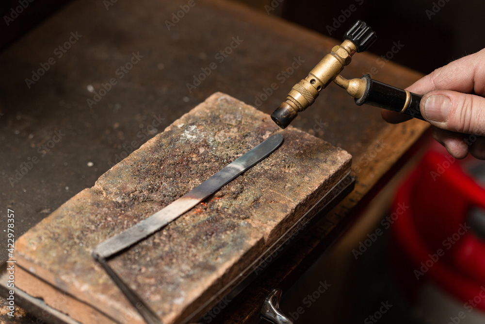 goldsmith jeweler heats a piece of silver with a gas torch to make a ring. goldsmith jeweler heats a piece of silver with a gas torch to make a ring.
