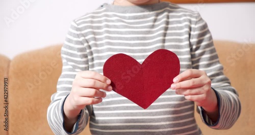 Close-up of child hands holding a red heart-shaped postcard and showing her to the camera. Valentine's day concept.