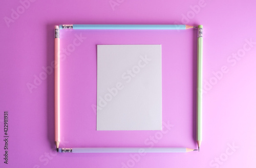 Composition frame with pencils and white paper, on purple background, pastel color and top view photo