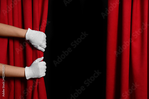 Woman opening red front curtains on black background, closeup. Space for text