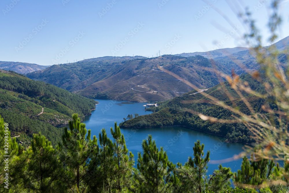 Sunny riverside mountains. River water. Blue lake. Nature. Peaceful landscape in the forest. Green trees outdoors. Trás-os-montes, Portugal. Montalegre
