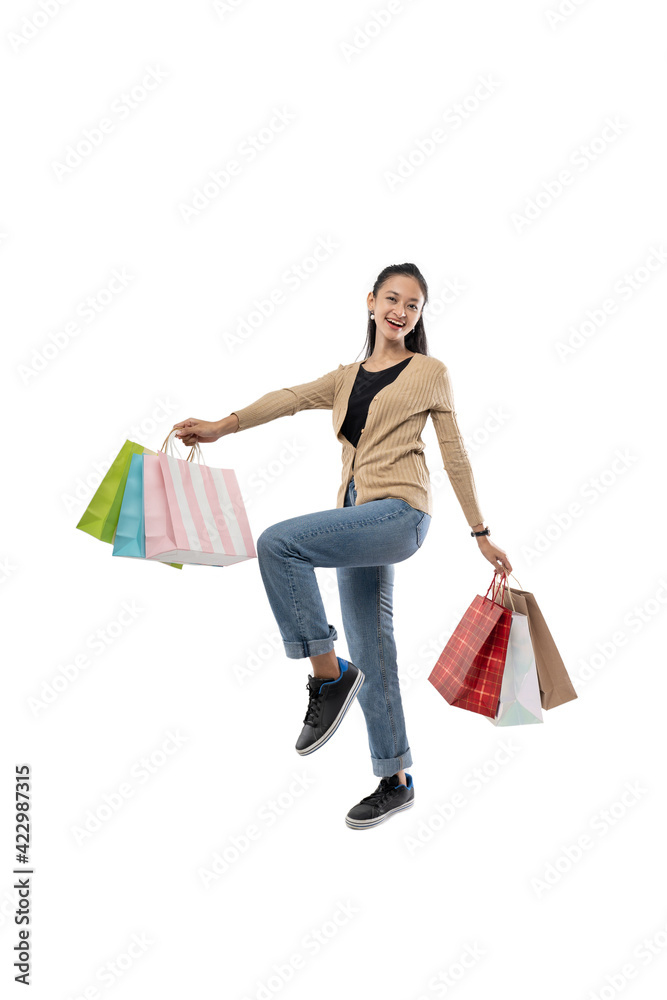 Beautiful and happy young Asian woman holding a shopping bag while raising one leg, isolated on white