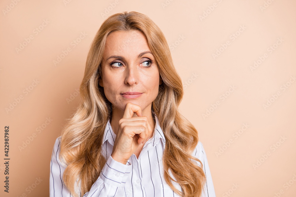 Photo of shiny cute mature lady wear striped shirt smiling finger chin looking empty space isolated beige color background