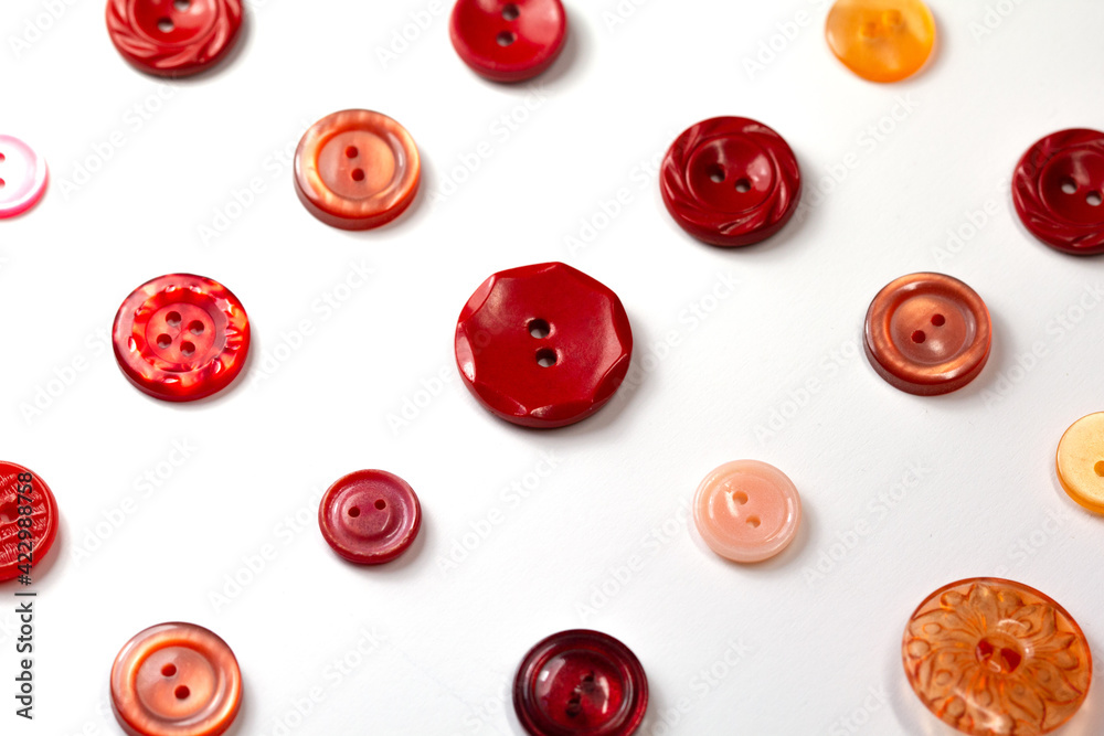Colorful red and pink buttons on a white background. Set of red buttons. Old vintage buttons close up. Copy space. Top view. Background of buttons. Colorful red and pink buttons on a white background. Set of red buttons. Old vintage buttons close up. Copy space. Top view. Background of buttons.