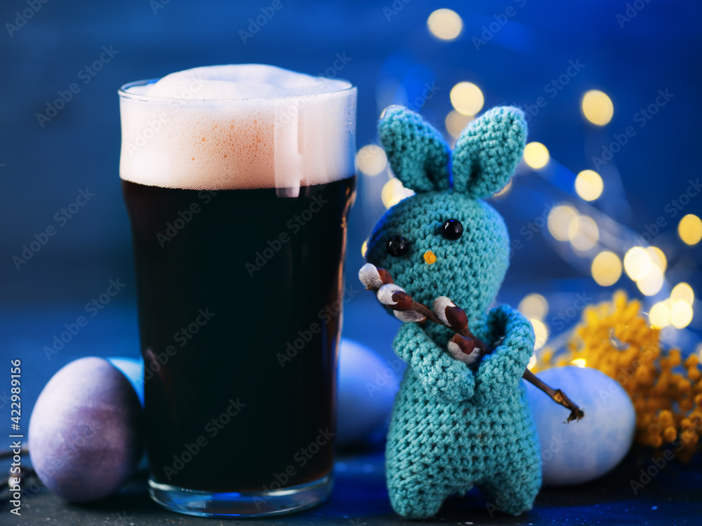 A glass of dark craft beer, Easter colored eggs, handmade knitted bunny with willow branch, celebrate Easter concept - obrazy, fototapety, plakaty 