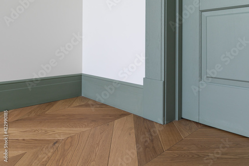 Fragment of classic interior with french herringbone parquet floor and green door and skirting boards. The final stage of finishing works in the apartment photo