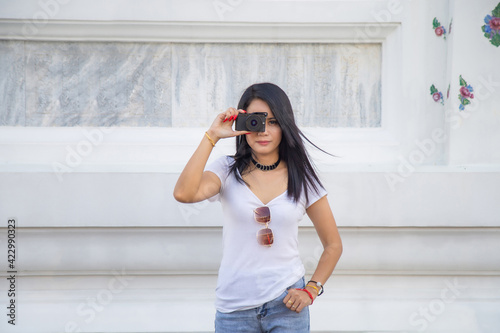 Portrait beautiful Asian woman in a white T-shirt taking a photo directly aimed at the viewer with a white wall in The temple in Thailand