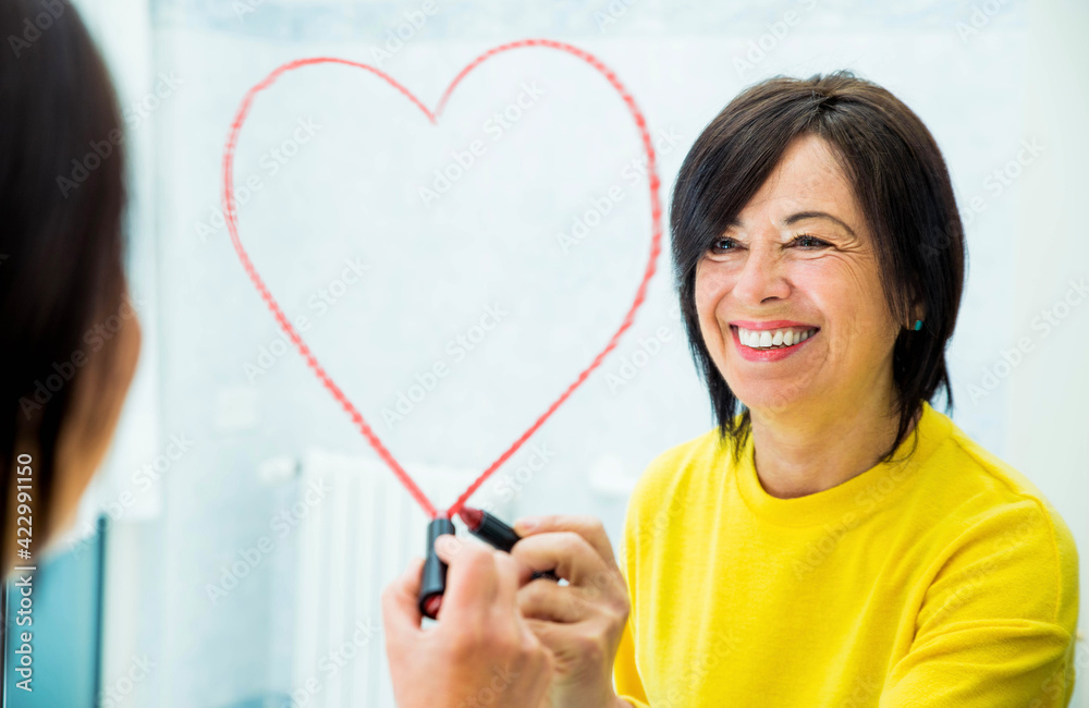 Positive senior woman drawing heart shape on the mirror at home - Self love and self care concept Positive senior woman drawing heart shape on the mirror at home - Self love and self care concept