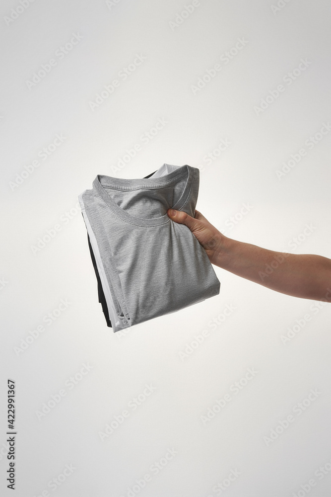 Male hand holding a stack of basic t-shirts against grey background