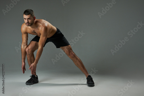 Strong athlete man with powerful torso warming up isolated on grey background