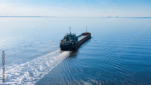 A large sea vessel goes by the sea in sunny calm weather, aerial view