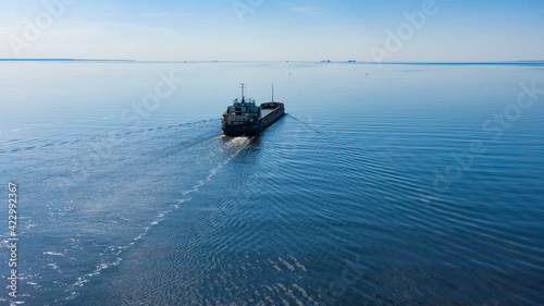 A large sea vessel goes by the sea in sunny calm weather, aerial view
