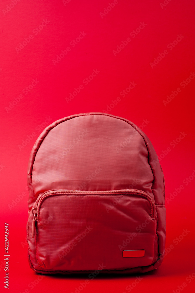 Children's backpack in pink fabric with shoulder straps, shot against a rich red background. Children's backpack in pink fabric with shoulder straps, shot against a rich red background.