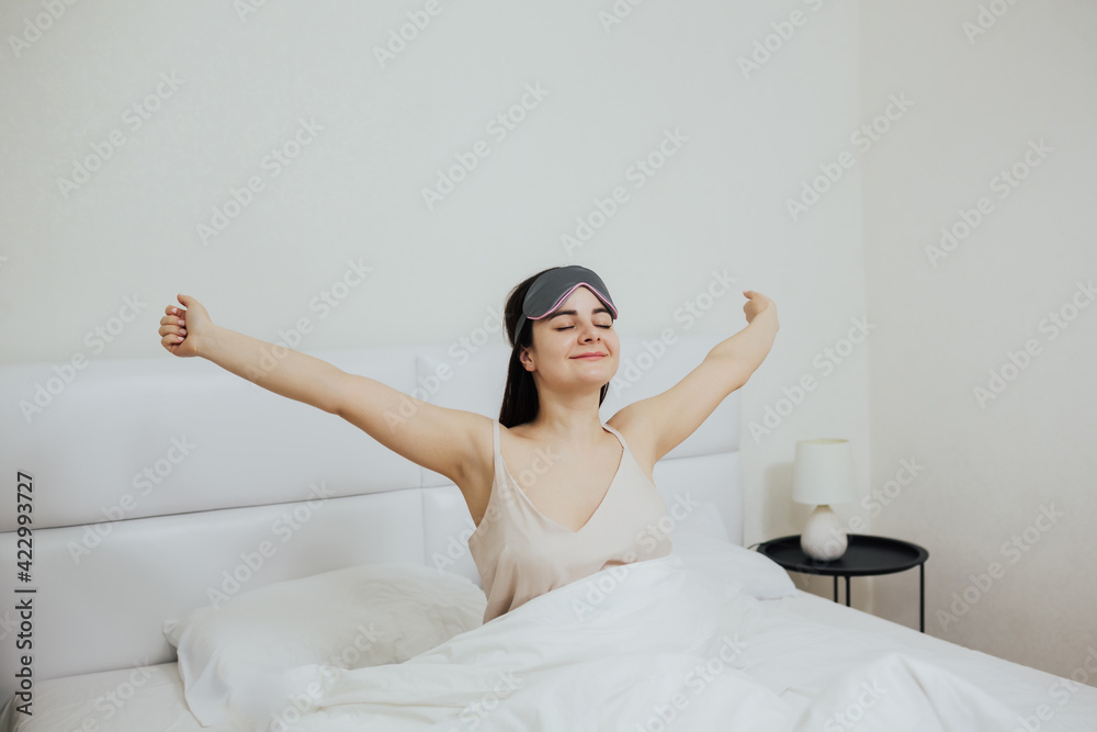 Young smiling woman with sleep mask waking up happily and stretching arms after a good night sleep. Young smiling woman with sleep mask waking up happily and stretching arms after a good night sleep.