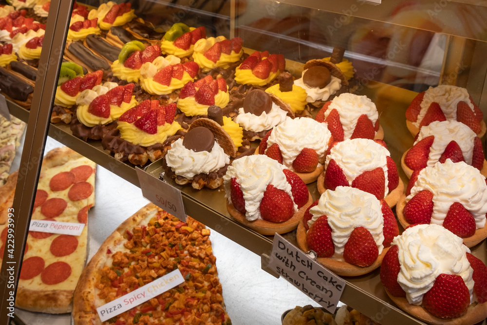 Fresh delicious sweet cakes with strawberries are in the store behind a glass window