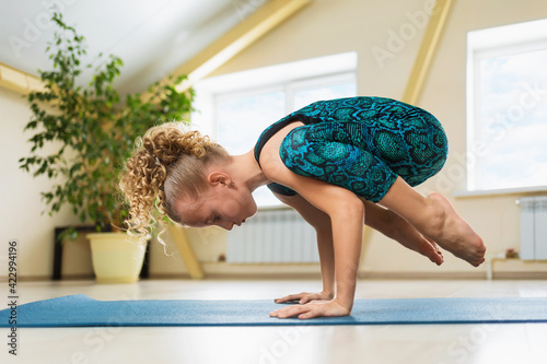 Little beautiful girl with blond hair practicing yoga doing handstand exercise, kakasana or crow pose on a gymnastic mat in the studio photo