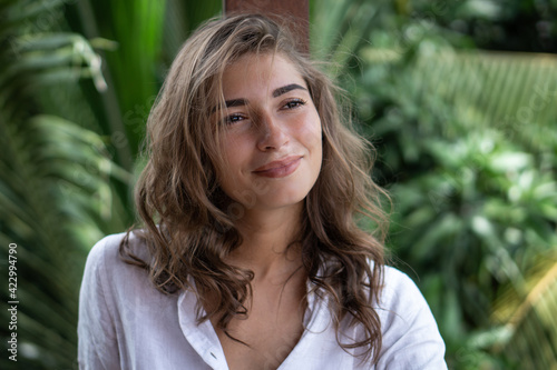 Portrait of young beautiful woman close up in white shirt on balcony of tropical bungalow with palm trees view