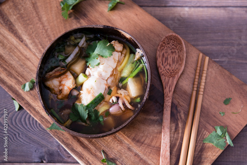 Asian soup with halibut and seafood (hemultan) shrimps, mussels and young octopus. Korean traditional soup on a dark wooden background with herbs. Wooden plate and spoon. photo