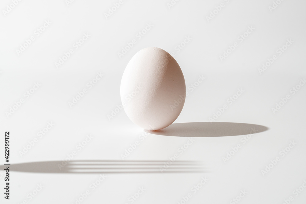 A standing egg and shadow of a fork on white background - obrazy, fototapety, plakaty 
